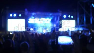 人们在摇滚音乐会上挥舞双手，粉丝记录视频并在android上拍照，在音乐会上，
